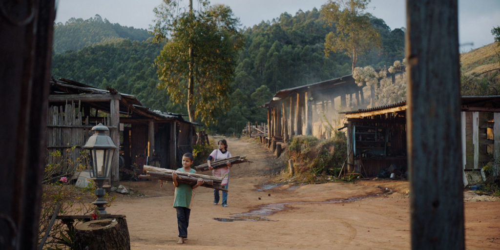 Charcoal film photo of a child carrying wood in a village.